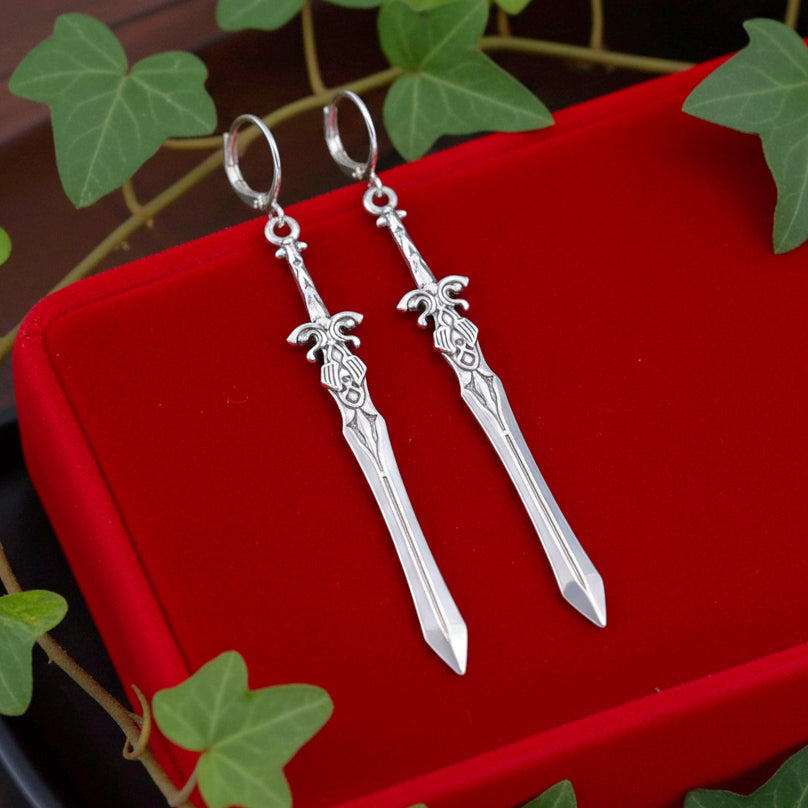 Fantasy silver sword earrings with hoopson a red surface with green leaves in the background