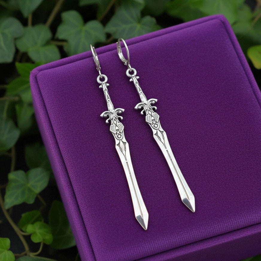 Silver sword-shaped earrings on a purple cushion with green leaves in the background