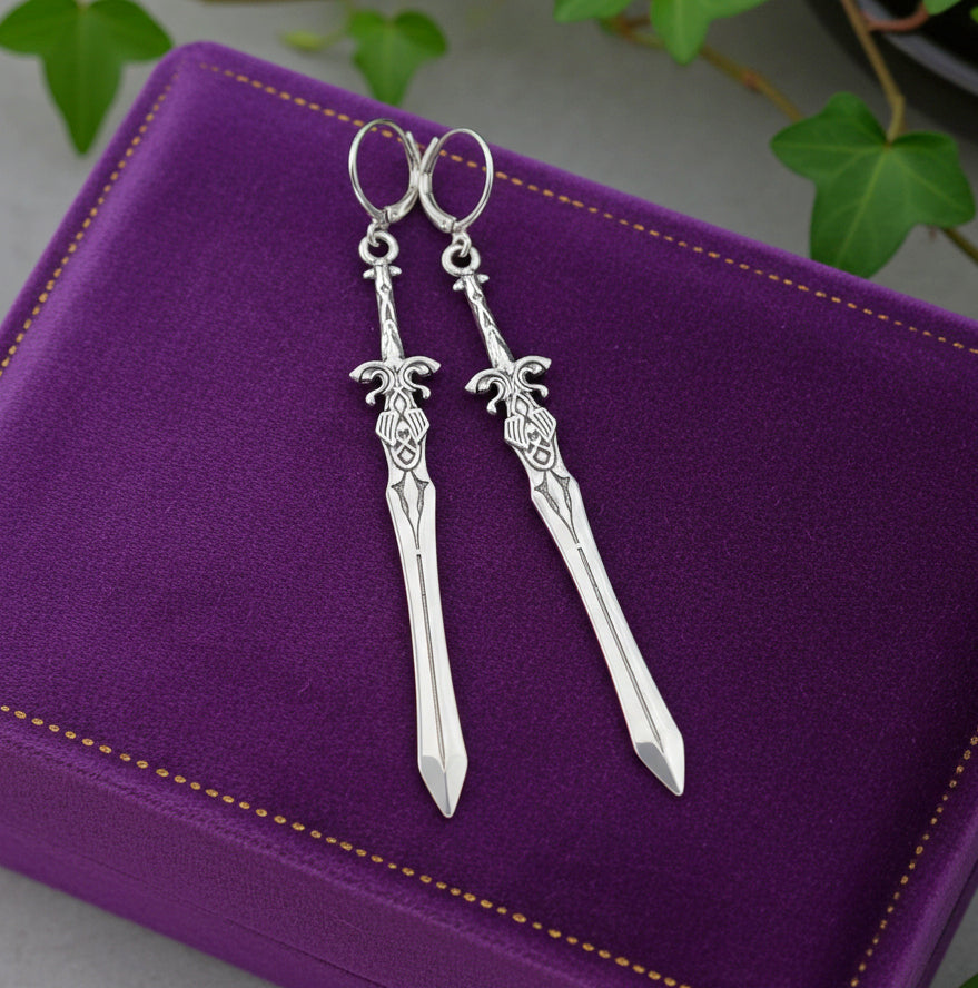 Silver sword-shaped earrings on a purple cushion with green leaves in the background