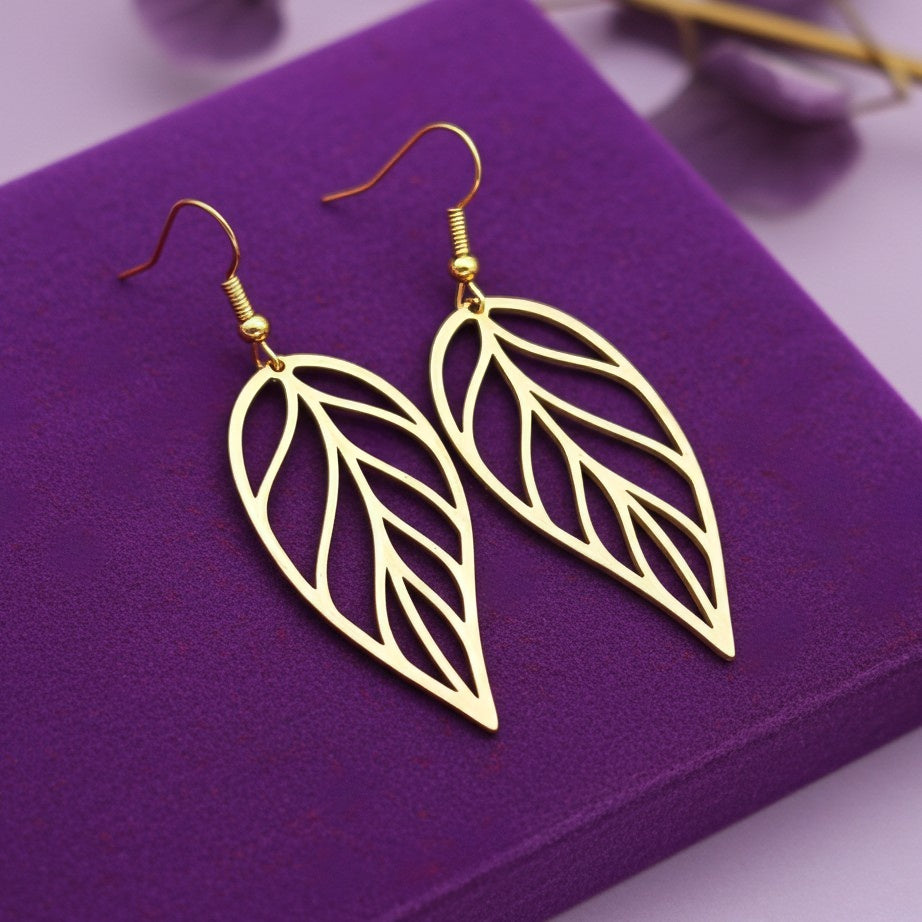 Large gold stainless steel leaf earrings with hooks on a purple background