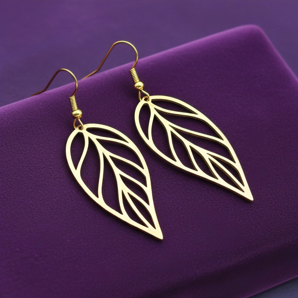 Large gold stainless steel leaf earrings with hooks on a purple background