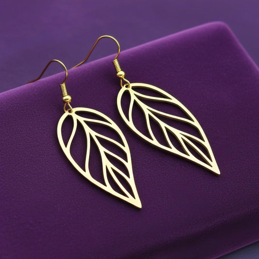Large gold stainless steel leaf earrings with hooks on a purple background