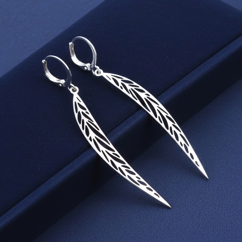 Long pointy stainless steel leaf earrings with silver hoops on a blue background