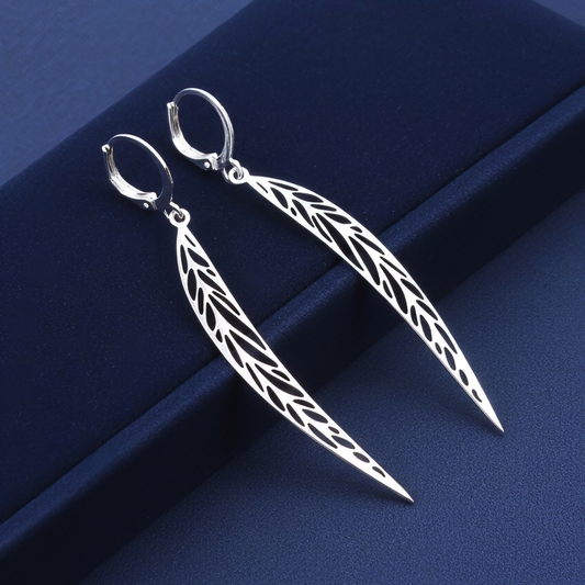 Long pointy stainless steel leaf earrings with silver hoops on a blue background