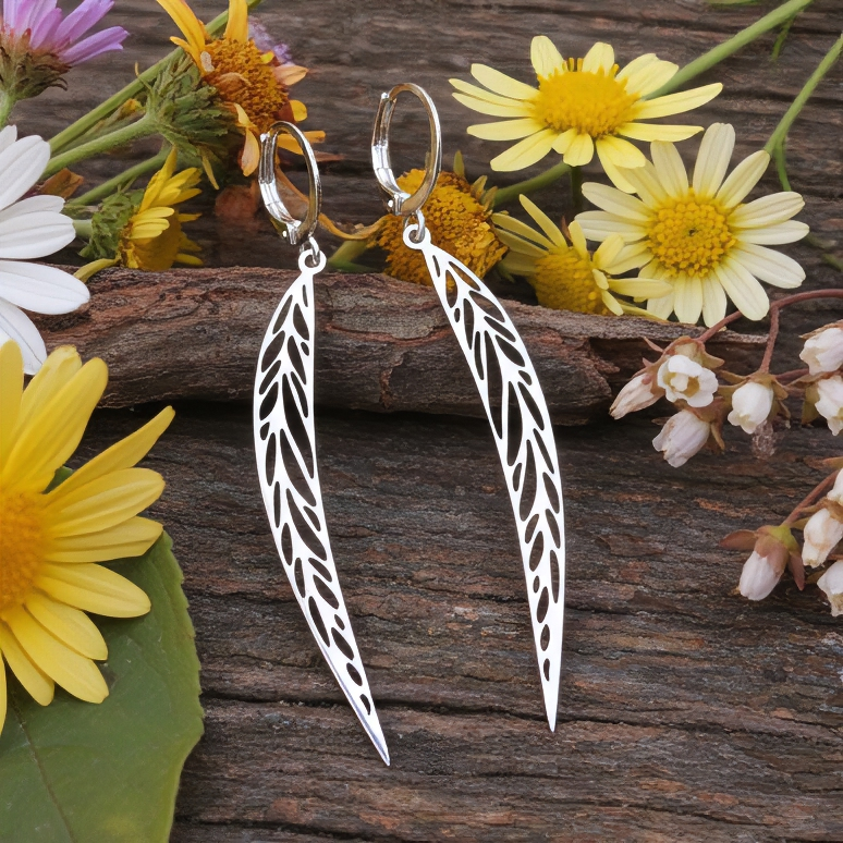 Long pointy stainless steel leaf earrings with silver hoops on a wood background with flowers