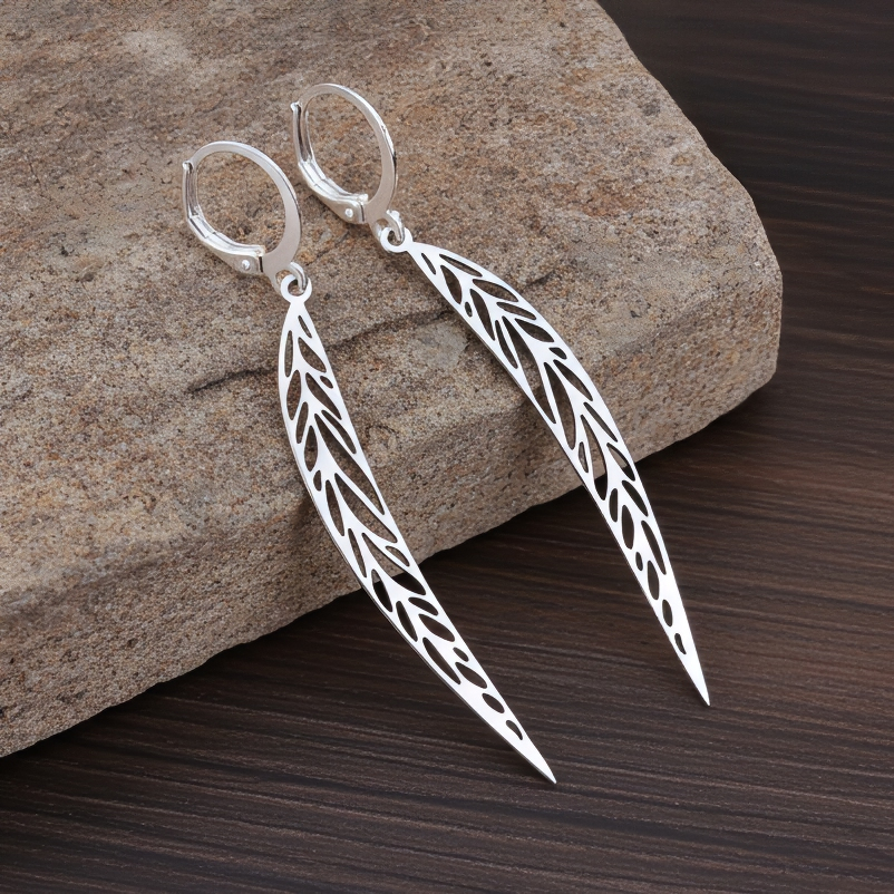 Long pointy stainless steel leaf earrings with silver hoops on a stone background