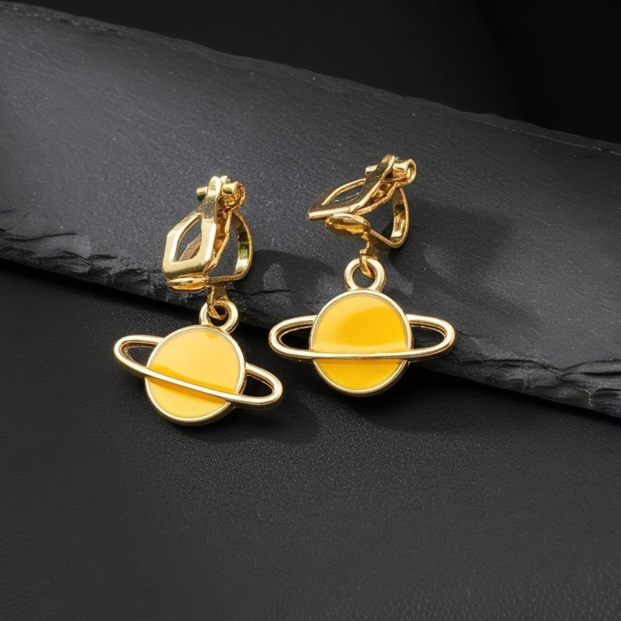 Yellow Saturn planet earrings with gold clip-ons on a black background