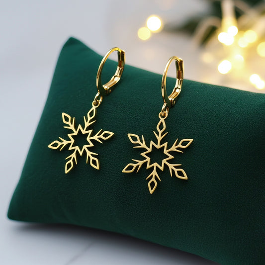 Gold snowflake earrings with hoops on a green fabric background with lights