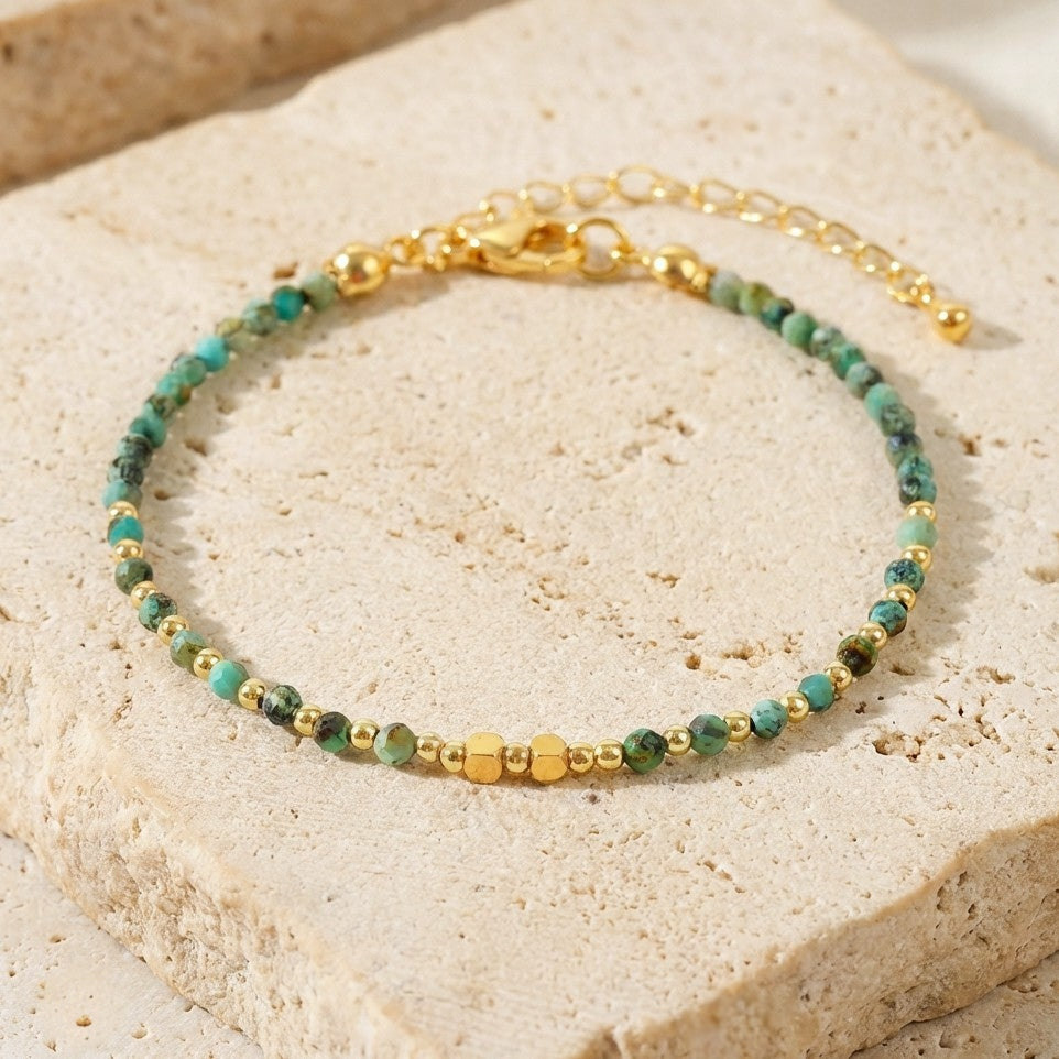 A dainty bead bracelet with faceted natural turquoise gemstone beads on a light stone background
