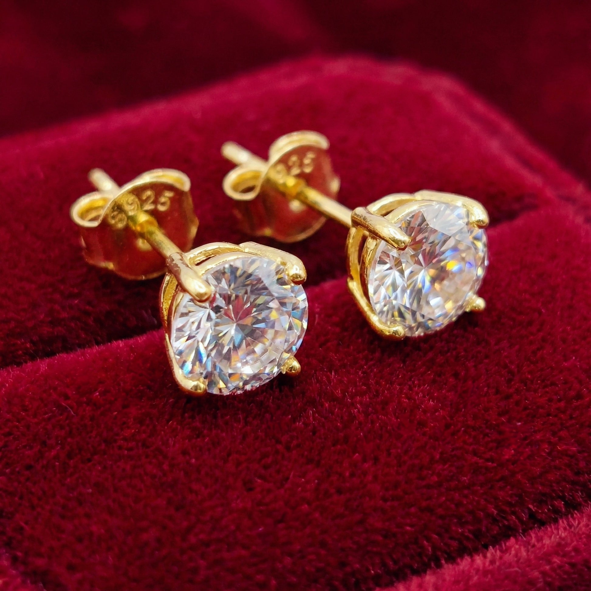 Sparkly gold 925 silver stud earrings with white cubic zirconia crystals on a red background