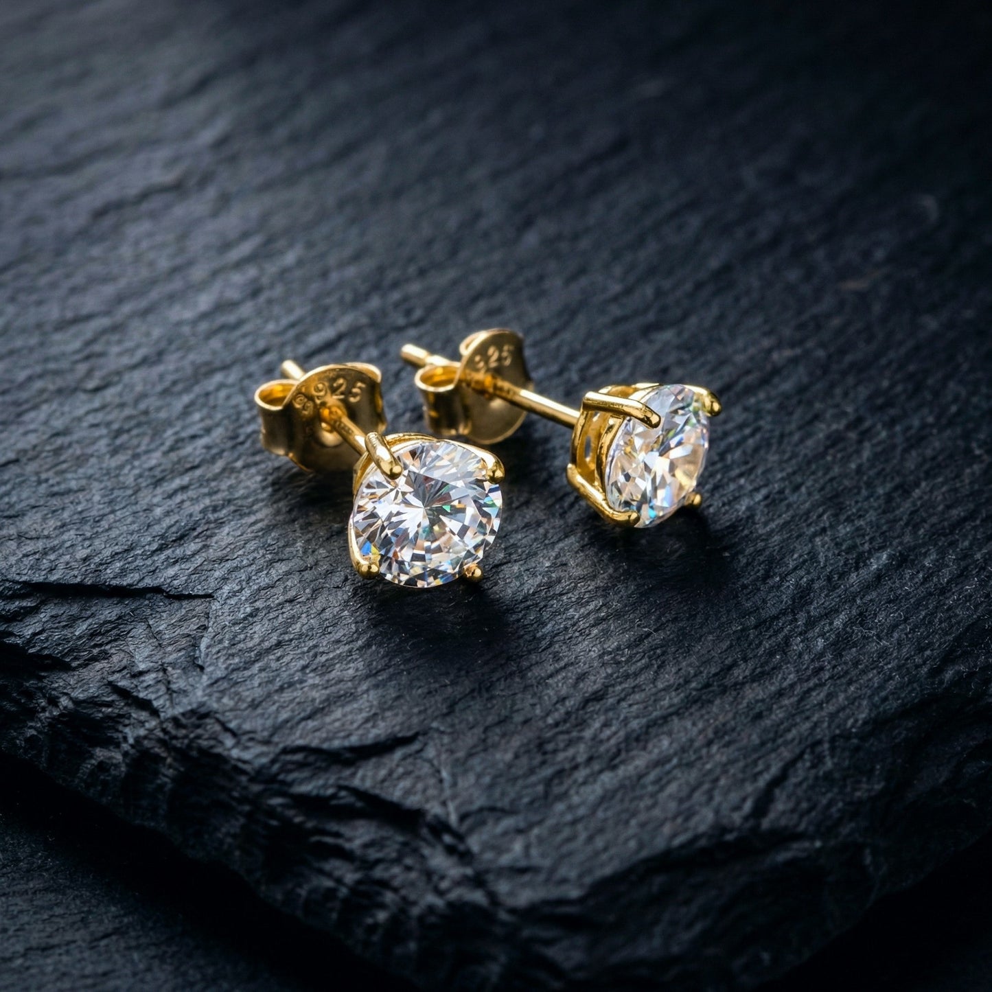 Sparkly gold 925 silver stud earrings with white cubic zirconia crystals on a dark stone background