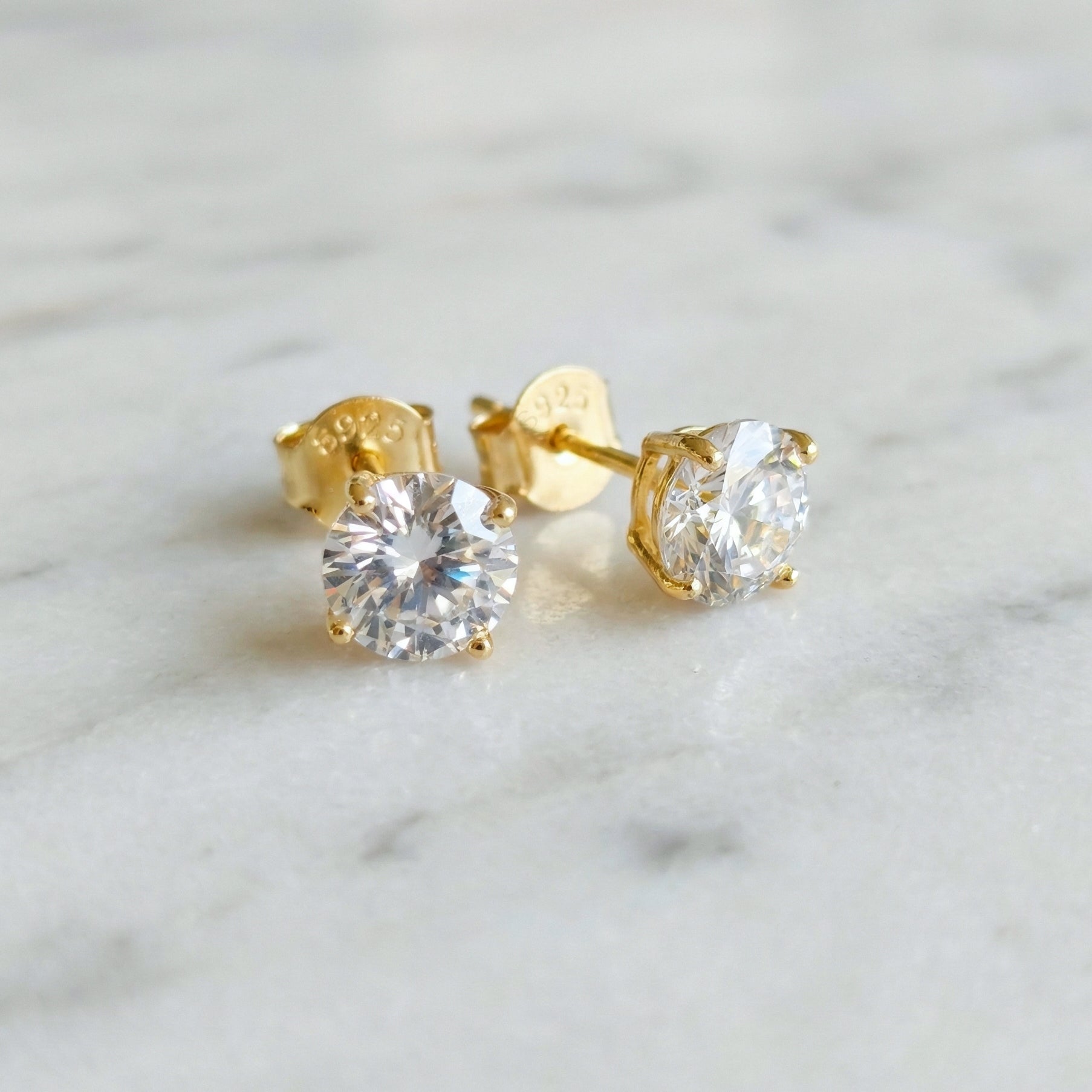 Sparkly gold 925 silver stud earrings with white cubic zirconia crystals on a marble background