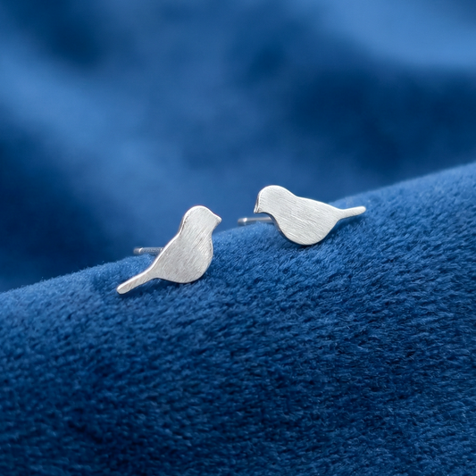 Bird stud earrings in a matte brushed silver, on a blue background