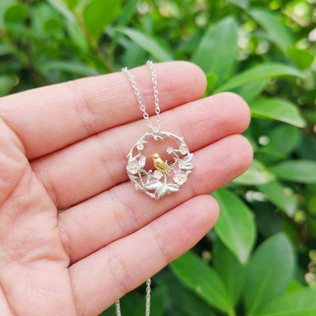 Silver necklace with a circular pendant featuring a bird held in a hand against a green leafy background
