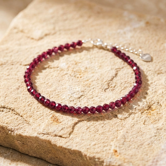Dark red natural garnet gemstone bead bracelet on a light stone background. The beads are faceted and catch the light and the bracelet has an adjustable real 925 silver clasp.