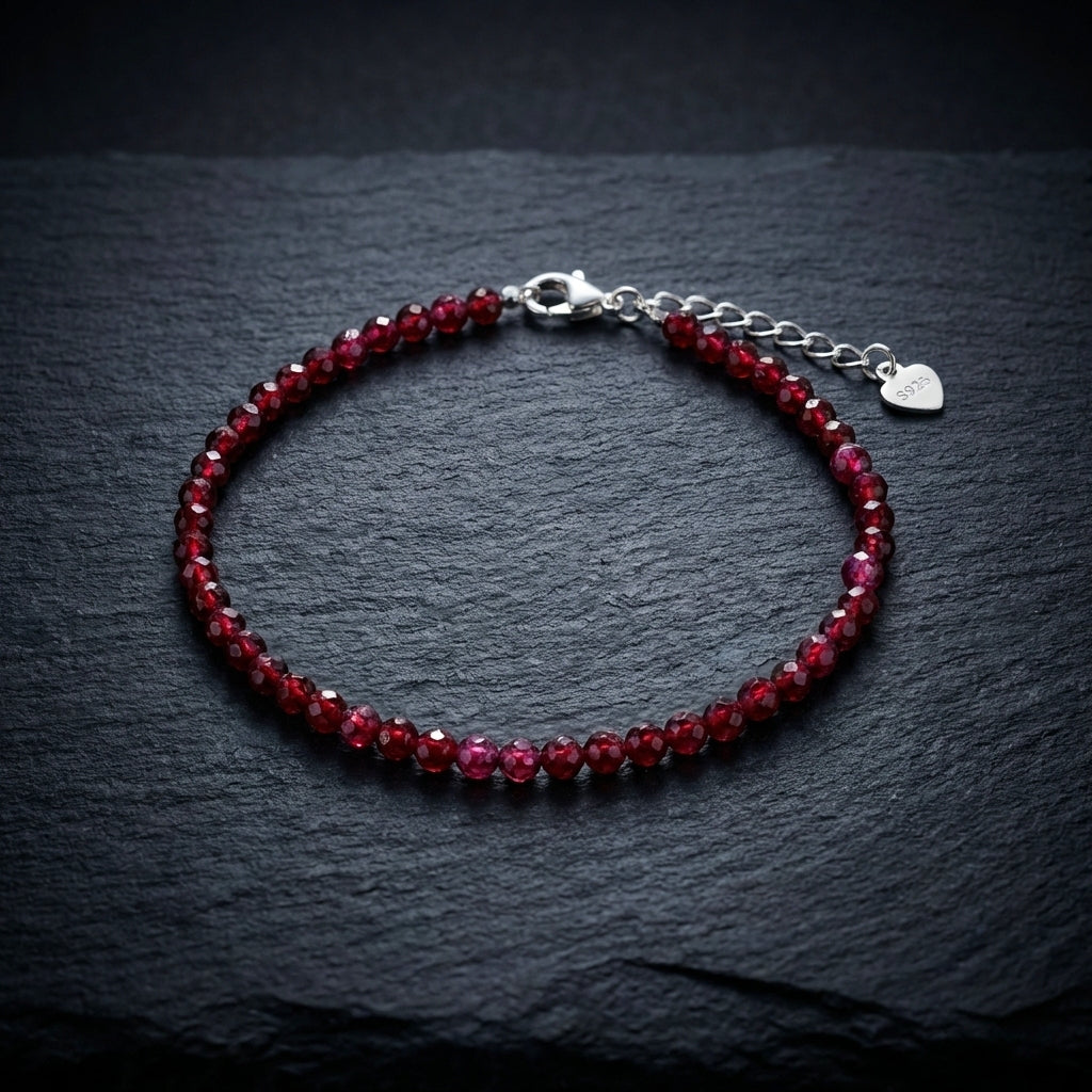 Dark red natural garnet gemstone bead bracelet on a black background. The beads are faceted and catch the light and the bracelet has an adjustable real 925 silver clasp.