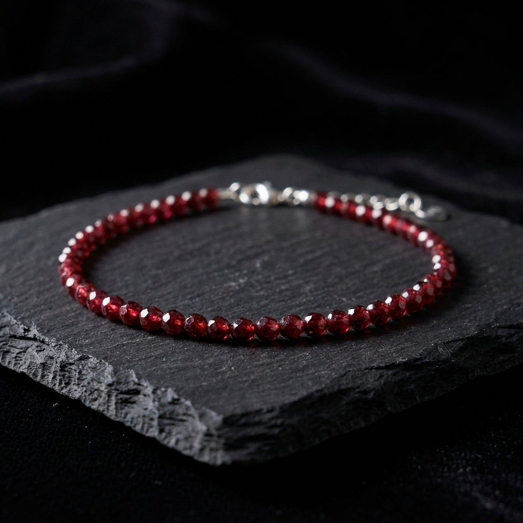 Dark red natural garnet gemstone bead bracelet on a black background. The beads are faceted and catch the light and the bracelet has an adjustable real 925 silver clasp.