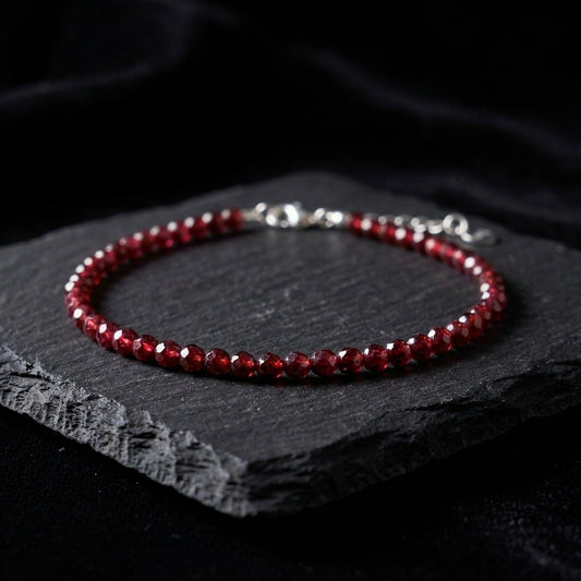 Dark red natural garnet gemstone bead bracelet on a black background. The beads are faceted and catch the light and the bracelet has an adjustable real 925 silver clasp.