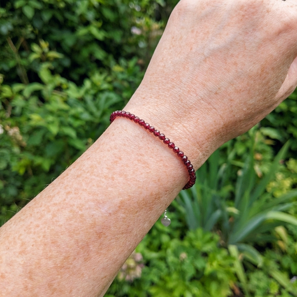 A wrist wearing a red natural garnet gemstone bead bracelet, with greenery behind