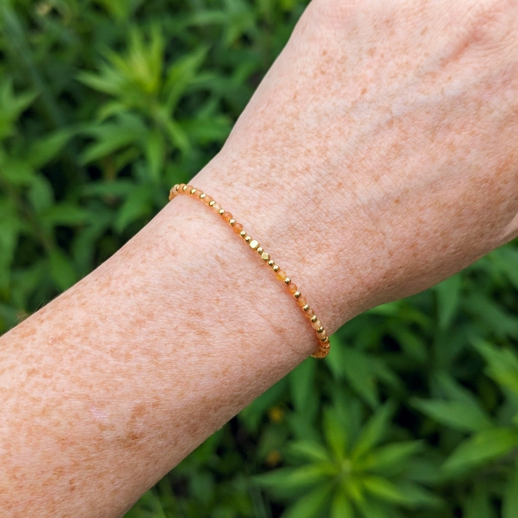 A wrist wearing a dainty yellow aventurine beaded boho bracelet with gold spacer beads and orange gemstone beads