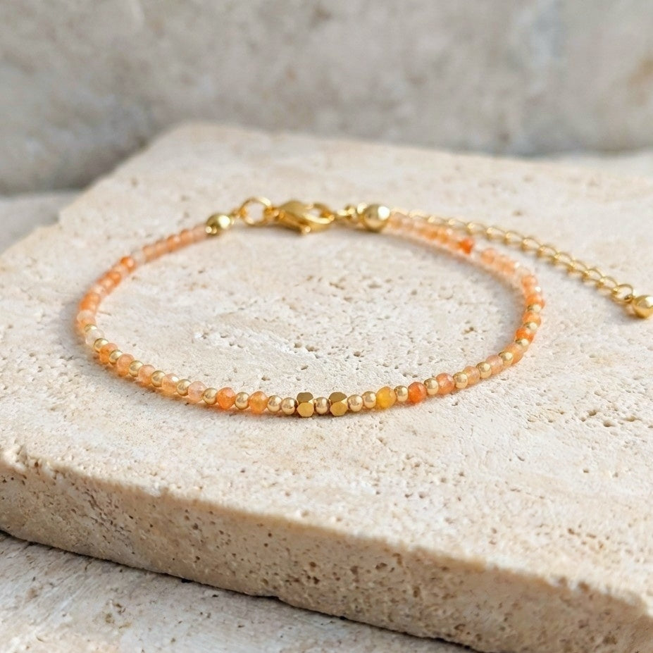 Yellow aventurine beaded boho bracelet with gold spacer beads and orange gemstone beads, on a light stone background