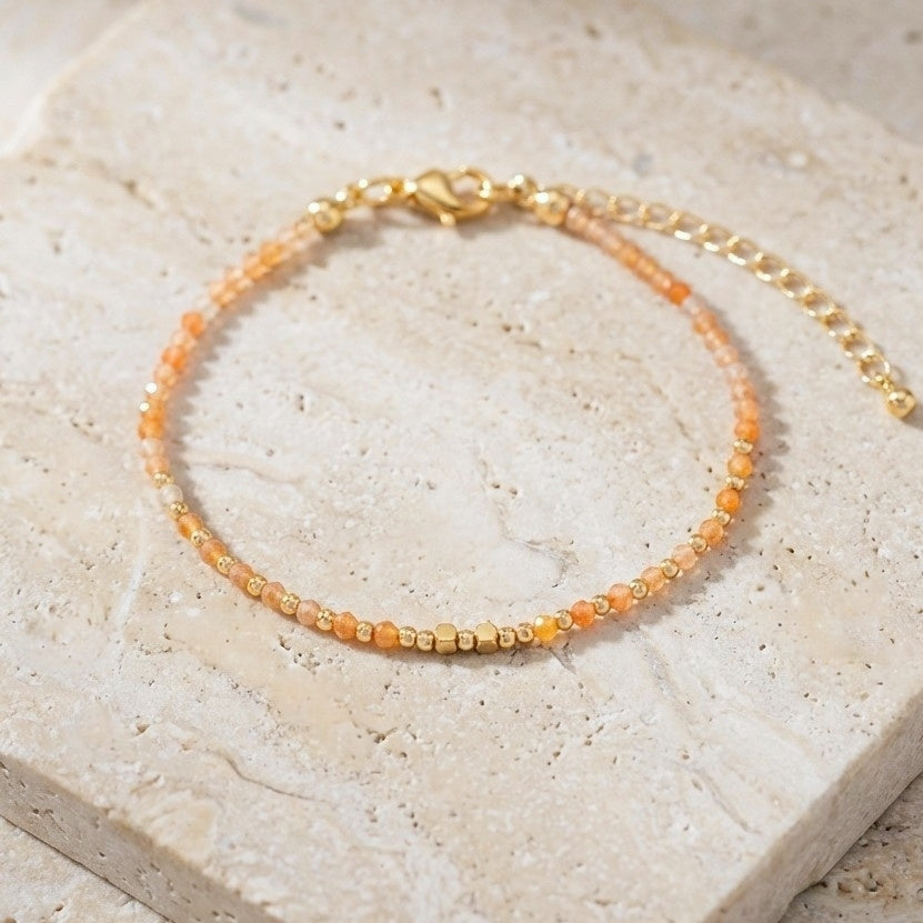 Yellow aventurine beaded boho bracelet with gold spacer beads and orange gemstone beads, on a light stone background