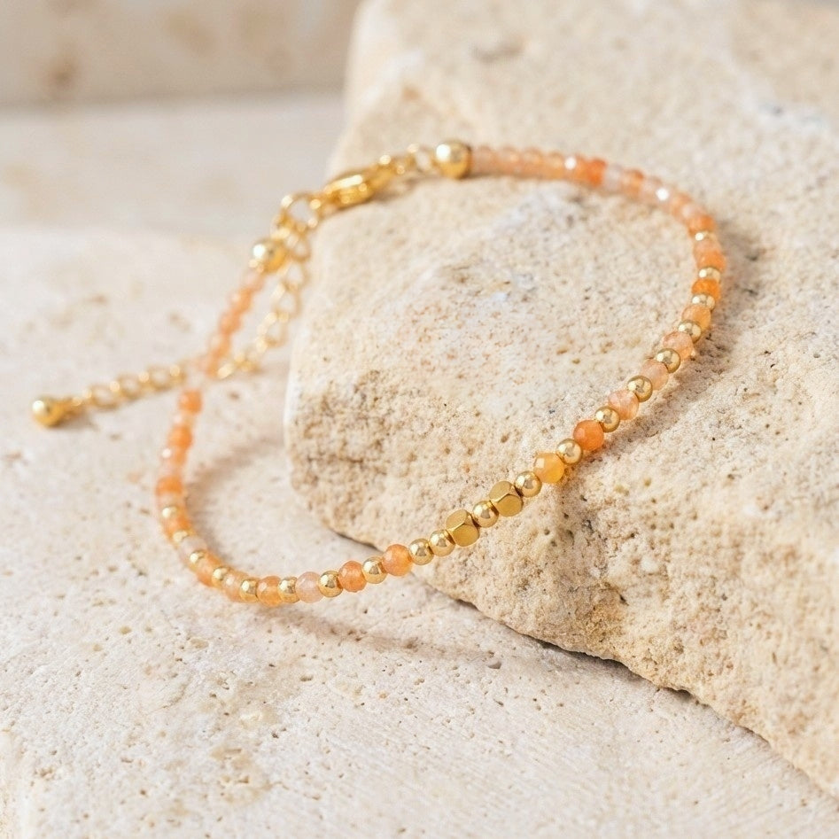 Yellow aventurine beaded boho bracelet with gold spacer beads and orange gemstone beads, on a light stone background