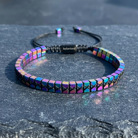 A men's metallic multicolour rainbow Hematite beaded bracelet with cube beads and adjustable cord on a stone surface