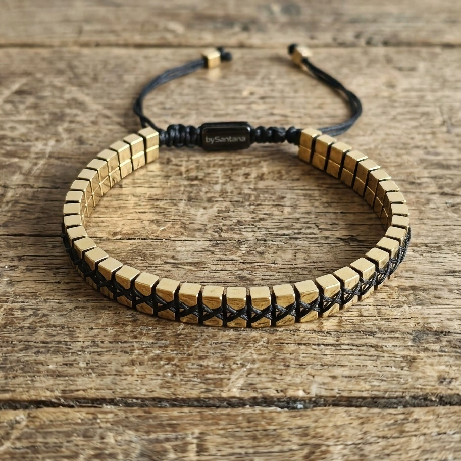 A men's metallic gold Hematite beaded bracelet with cube beads and adjustable cord on a wooden surface