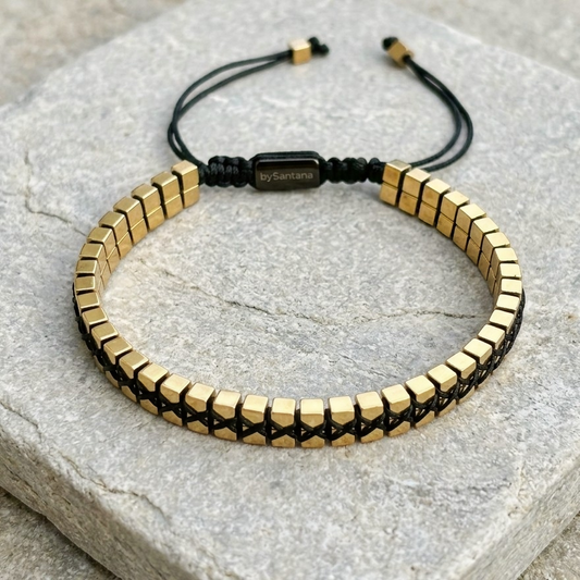 A men's metallic gold Hematite beaded bracelet with cube beads and adjustable cord on a stone surface