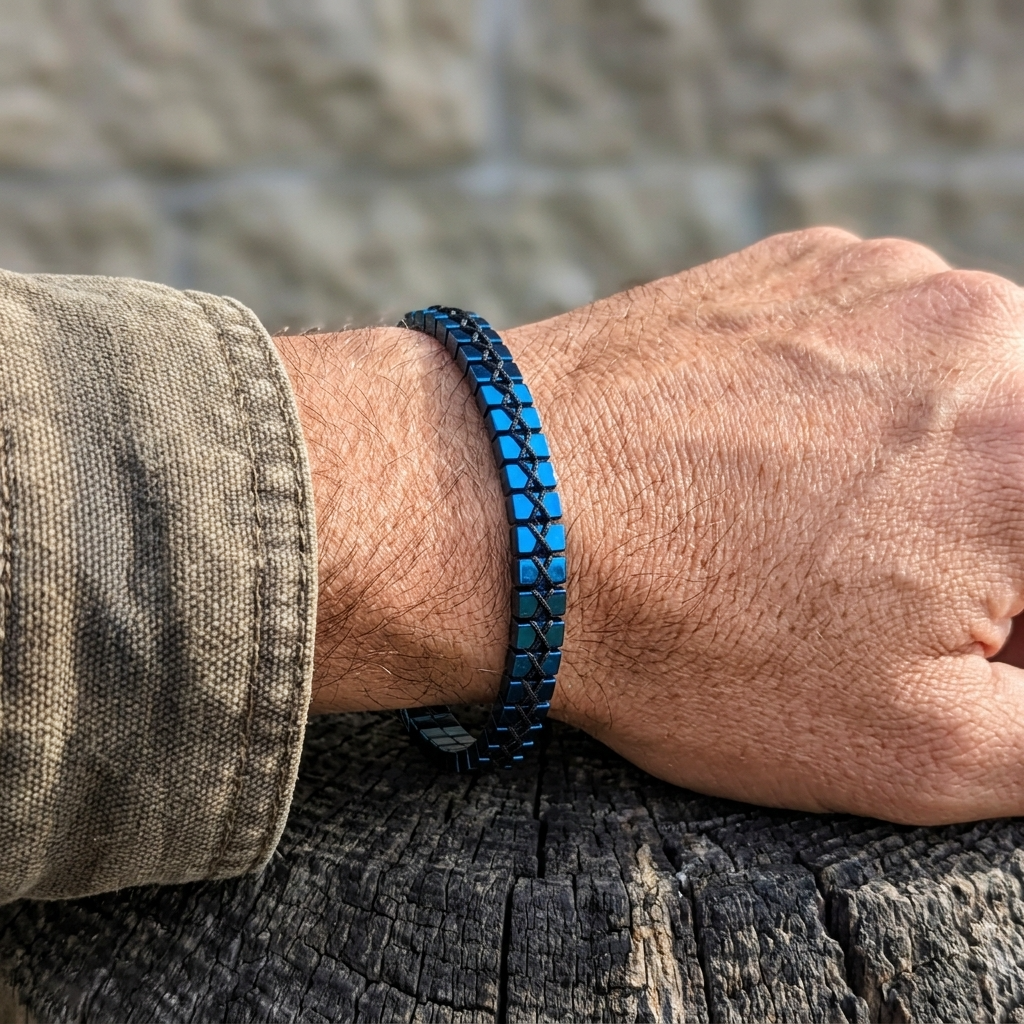 Man's hand wearing a blue Hematite woven bracelet with a blurred background