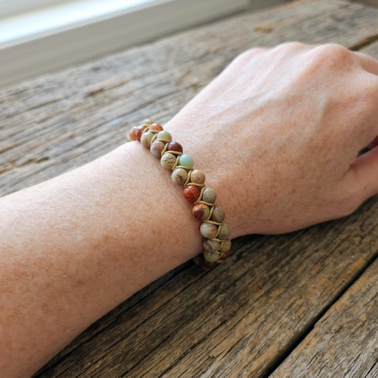 Shoushan Jasper or snakeskin jasper bead bracelet with a double layer of beads, woven together and an adjustable bolo drawstring. the beads are blue, red and beige with patterns. The natural gemstone bracelet is on a woman's wrist on a wooden table