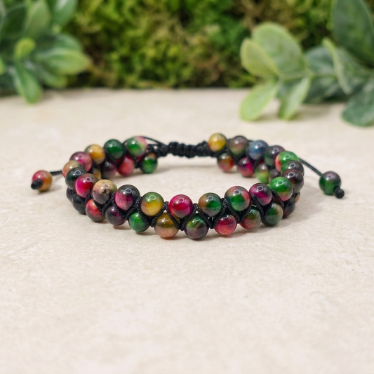 Colourful Tiger's Eye bracelet with a double row of pink, green and yellow gemstone beads, woven together with an adjustable drawstring. The bracelet sits on a light stone surface with greenery