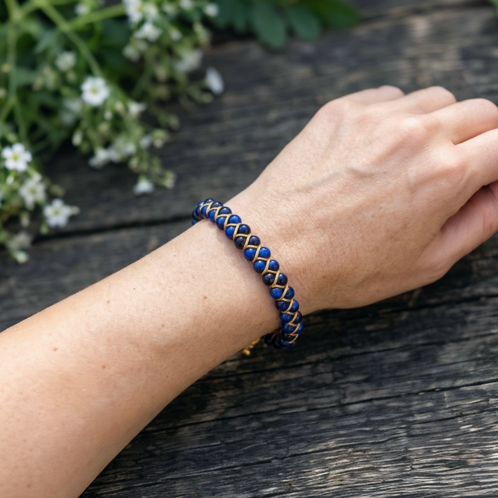 A woman's hand wearing a blue tigers eye beaded bracelet on a wooden surface with white flowers in the background