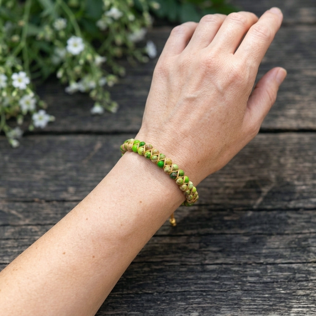 A woman's hand wearing a green beaded bracelet on a wooden surface with white flowers in the background