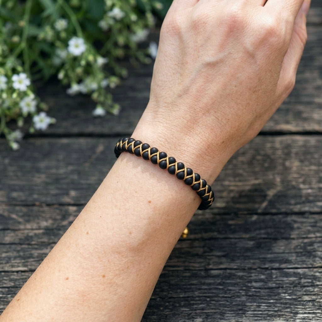 A woman's hand wearing a black onyx beaded bracelet on a wooden surface with flowers in the background