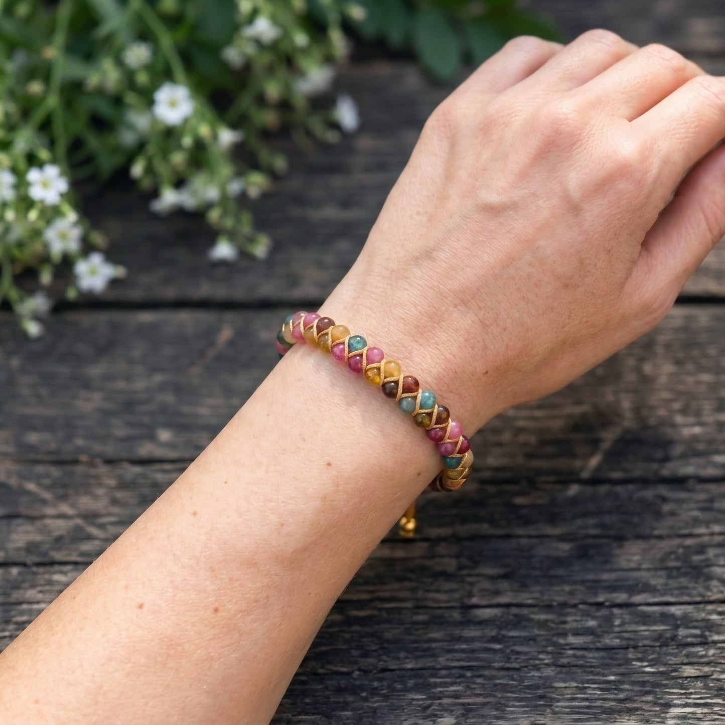 Multicolored beaded bracelet on a wrist with a wooden background and flowers.
