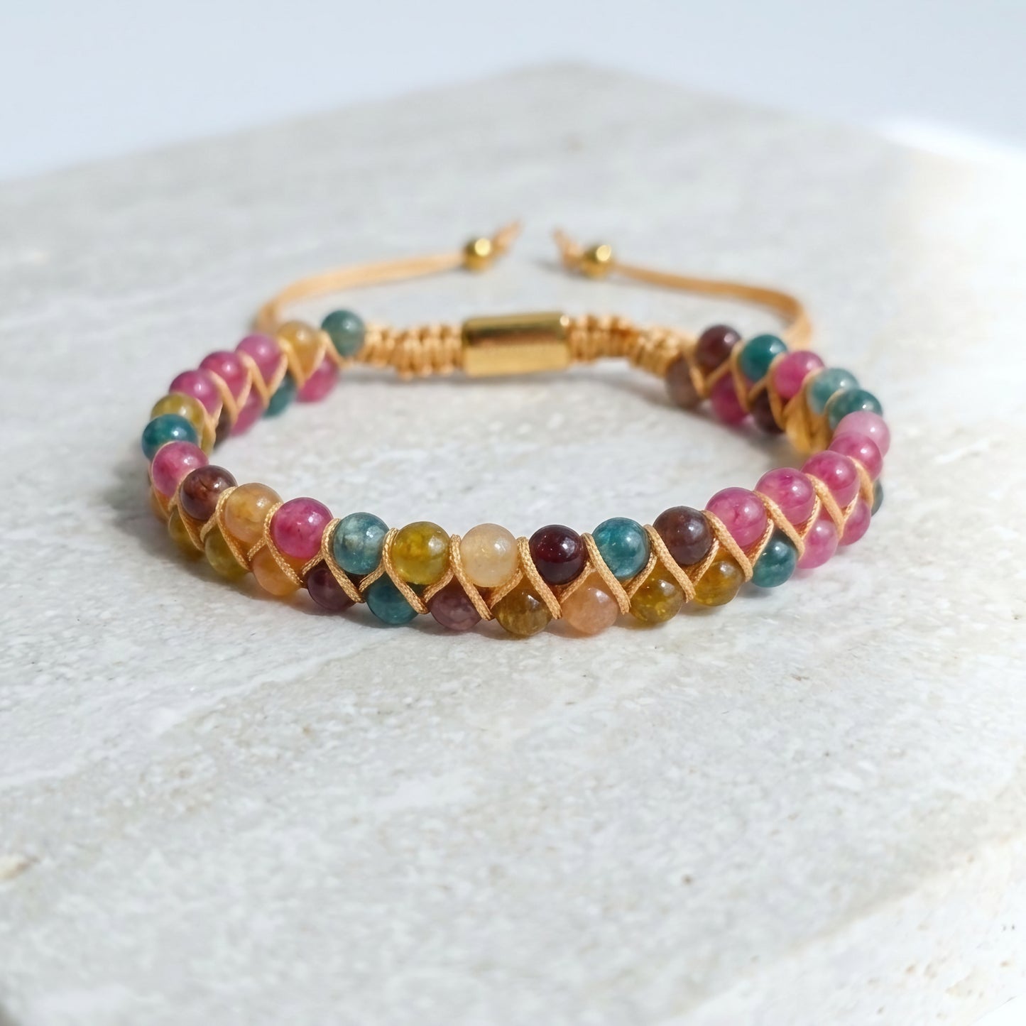 Multicolored Tourmaline beaded gemstone bracelet with beige cord wrapping on a light background