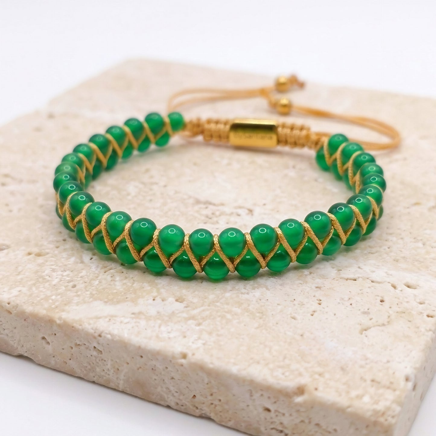 Green beaded bracelet with gold accents on a light stone surface