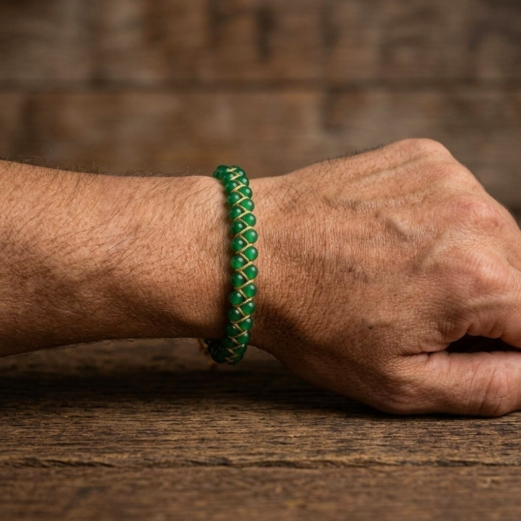 Man's hand wearing a green agate bead bracelet on a wooden surface with a blurred background