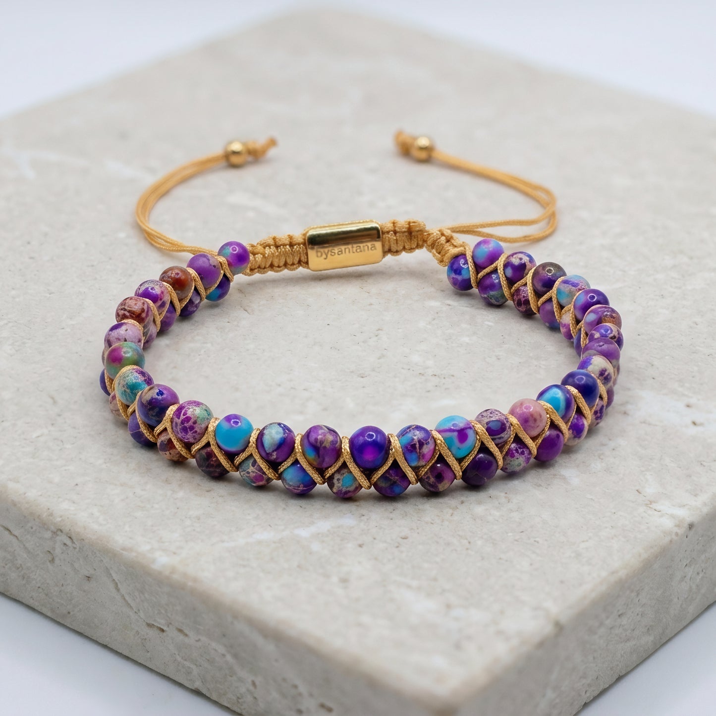 Galaxy sea sediment jasper bead bracelet on a marble surface. The colorful purple and blue gemstone beads are woven into a double row with an adjustable drawstring clasp.