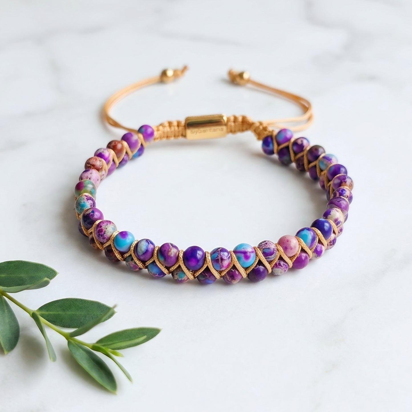 Galaxy sea sediment jasper bead bracelet on a marble surface. The colorful purple and blue gemstone beads are woven into a double row with an adjustable drawstring clasp.