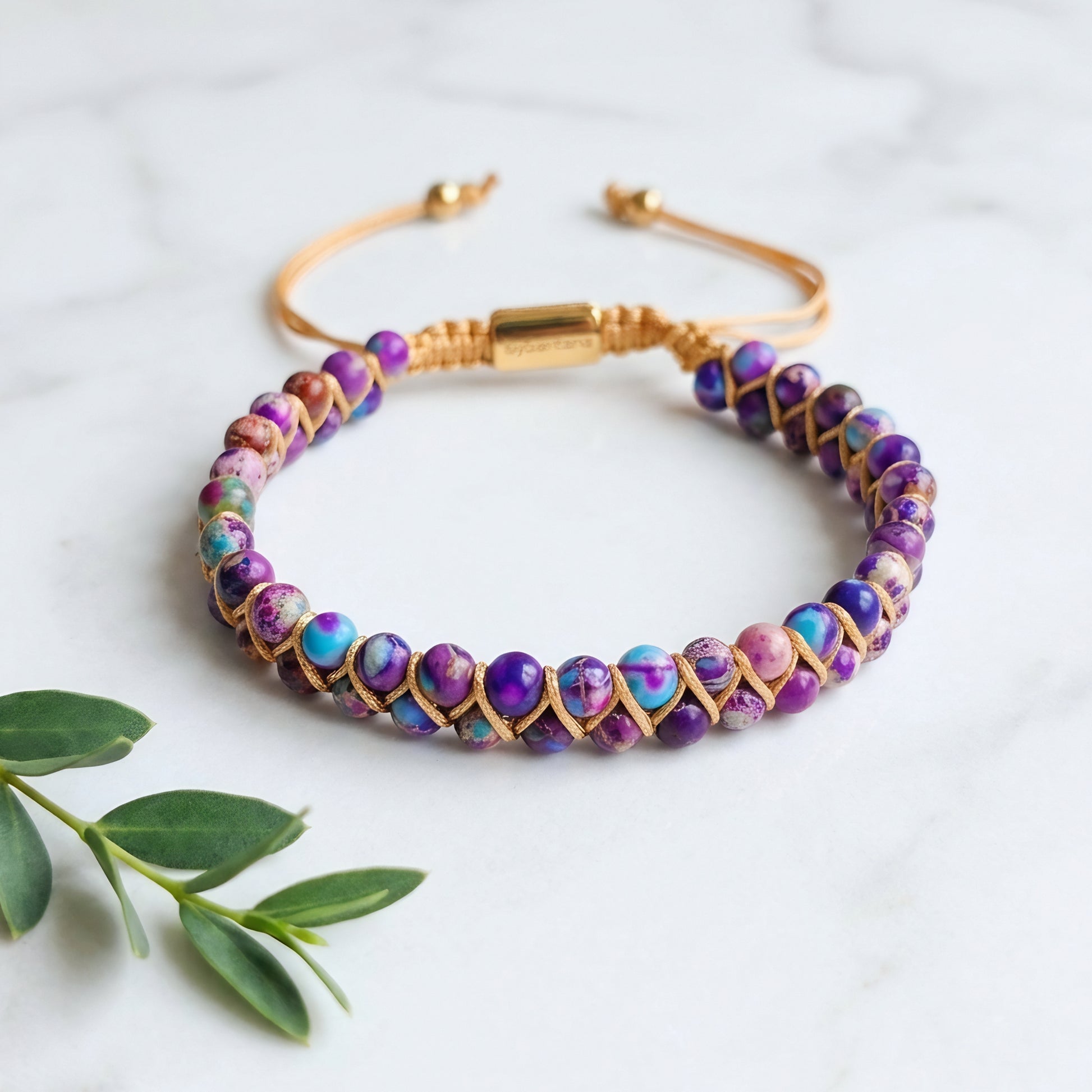 Galaxy sea sediment jasper bead bracelet on a marble surface. The colorful purple and blue gemstone beads are woven into a double row with an adjustable drawstring clasp.