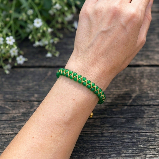 A woman's arm wearing a bold green agate gemstone beaded bracelet, woven with a double row of natural stone beads, on a wooden surface