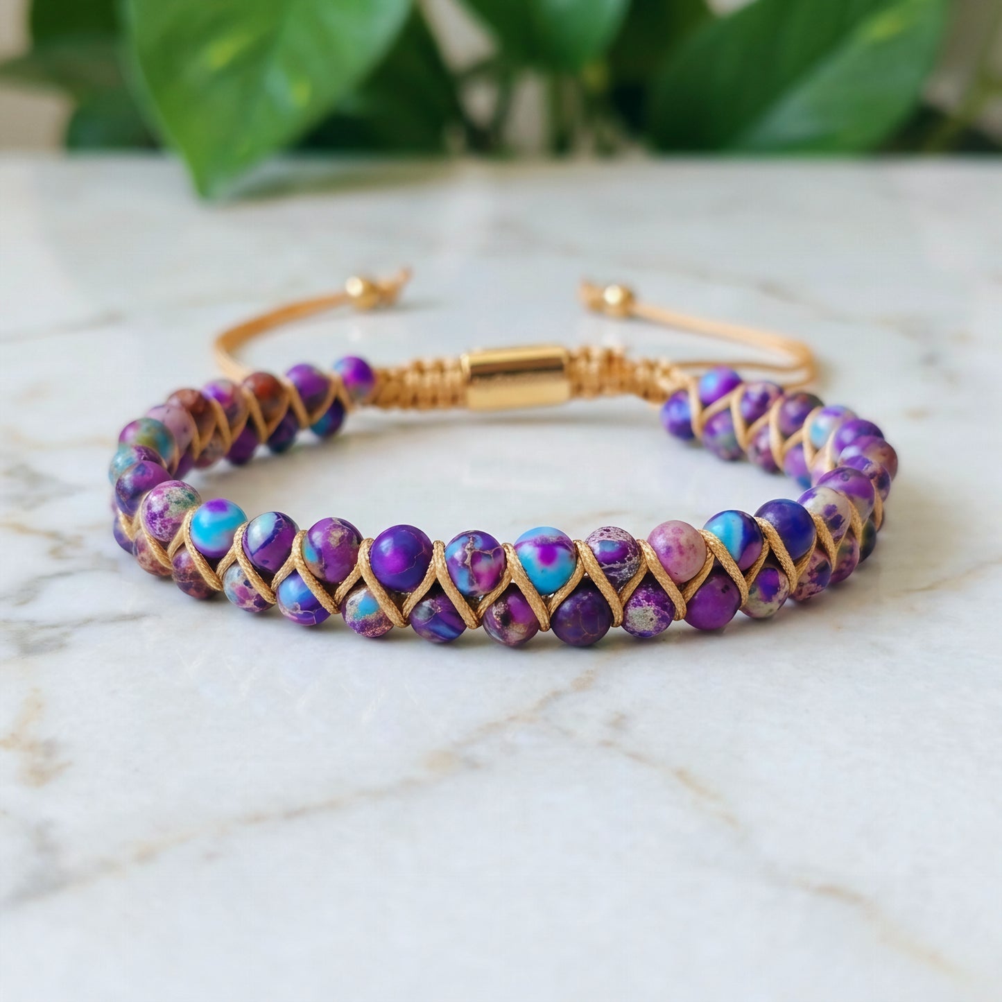 Galaxy sea sediment jasper bead bracelet on a marble surface. The colorful purple and blue gemstone beads are woven into a double row with an adjustable drawstring clasp.
