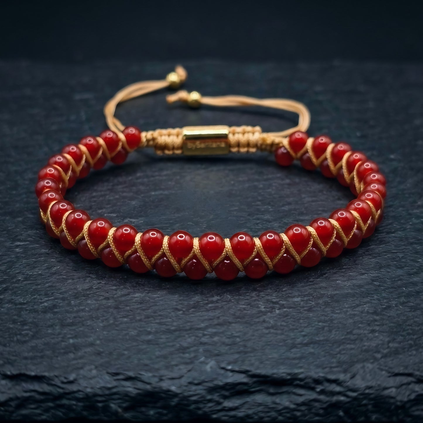 Bead bracelet with red agate gemstone beads in a double row, woven with an adjustable drawstring cord, on a dark stone surface 
