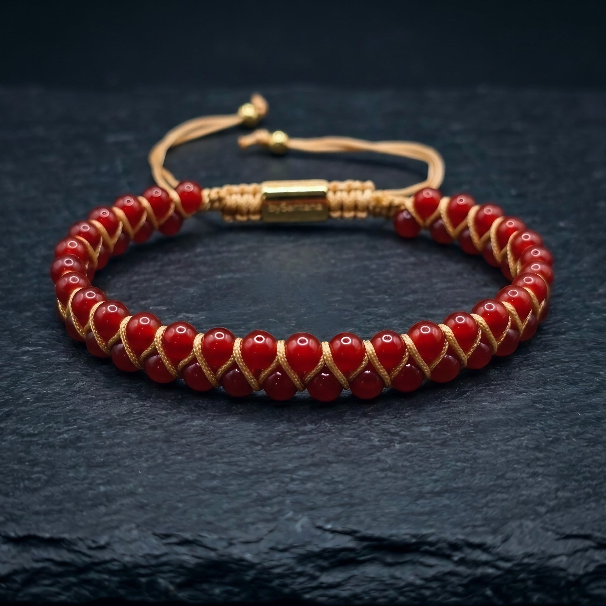 Bead bracelet with red agate gemstone beads in a double row, woven with an adjustable drawstring cord, on a dark stone surface 