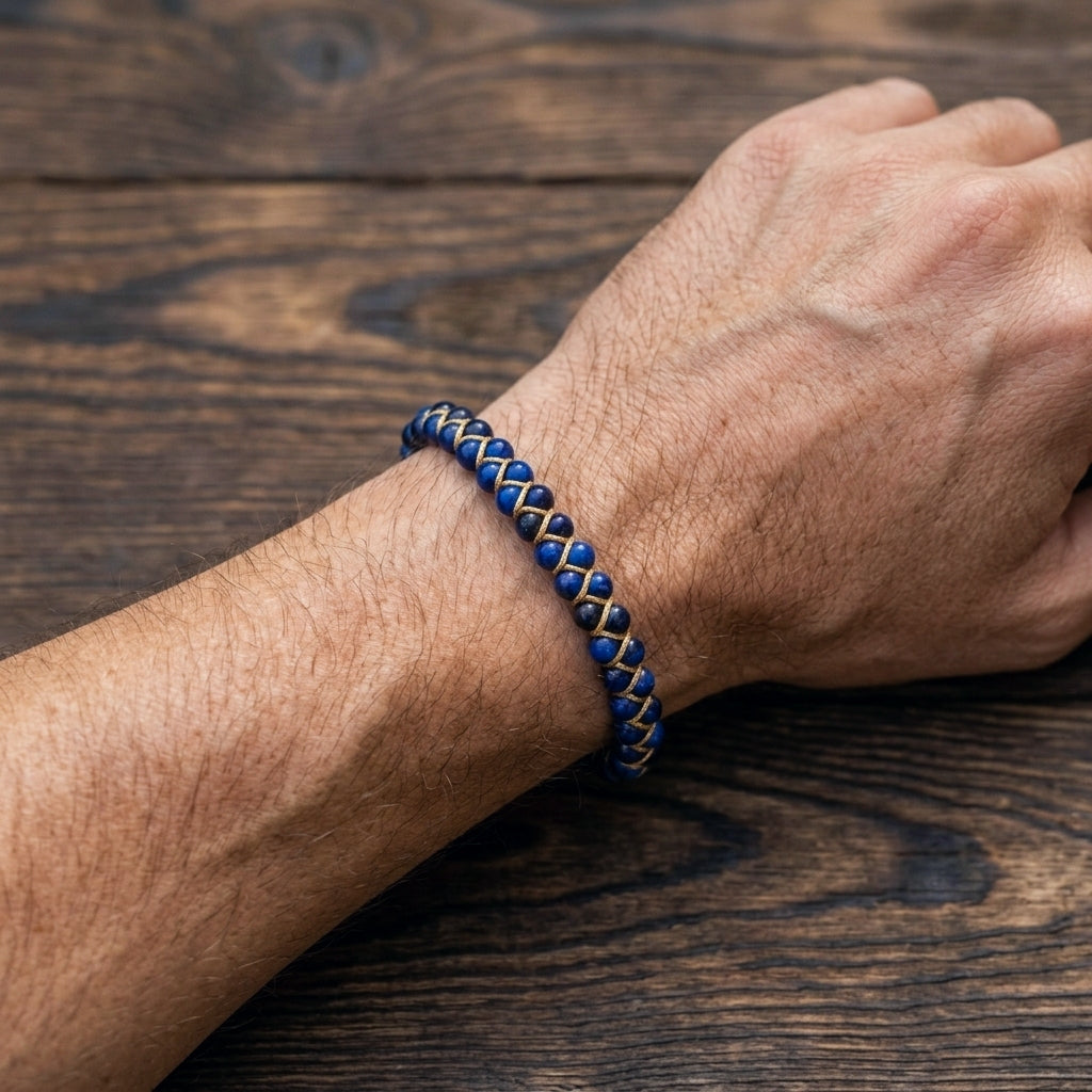 A man's hand wearing a blue tigers eye beaded bracelet on a wooden surface