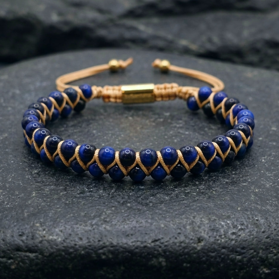 Woven bracelet with blue Tiger's Eye gemstone beads and gold accents on a dark stone surface