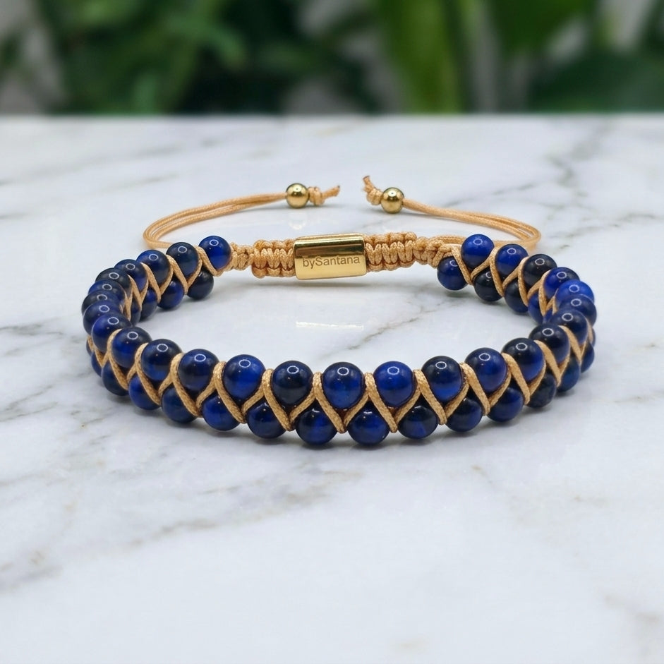 Woven bracelet with blue Tiger's Eye gemstone beads and gold accents on a light surface